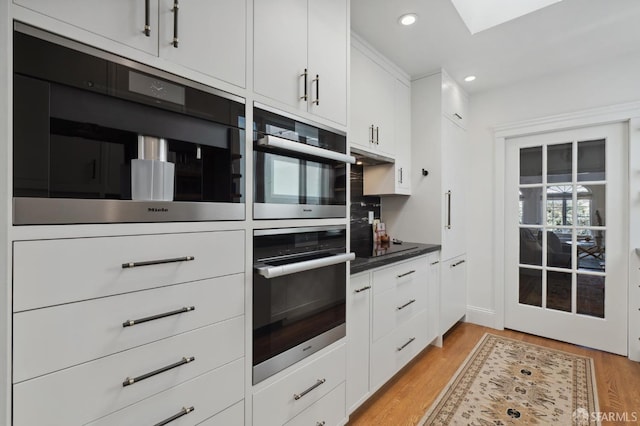 kitchen featuring light wood-type flooring, white cabinetry, a skylight, and recessed lighting