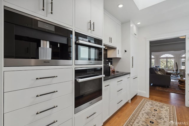 kitchen featuring white cabinetry, dark countertops, light wood-style flooring, recessed lighting, and a skylight