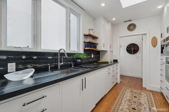 kitchen featuring a sink, white cabinetry, backsplash, light wood-style floors, and dark countertops