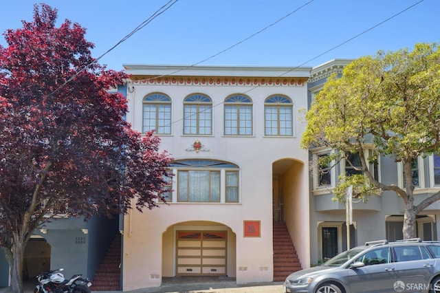 view of front facade with stucco siding, stairway, and a garage