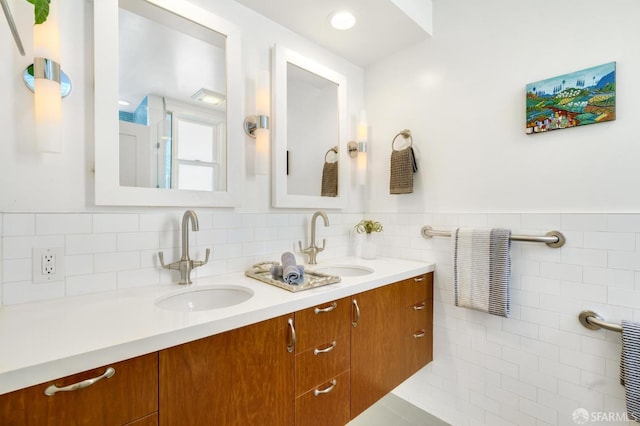 full bath with double vanity, tile walls, and a wainscoted wall