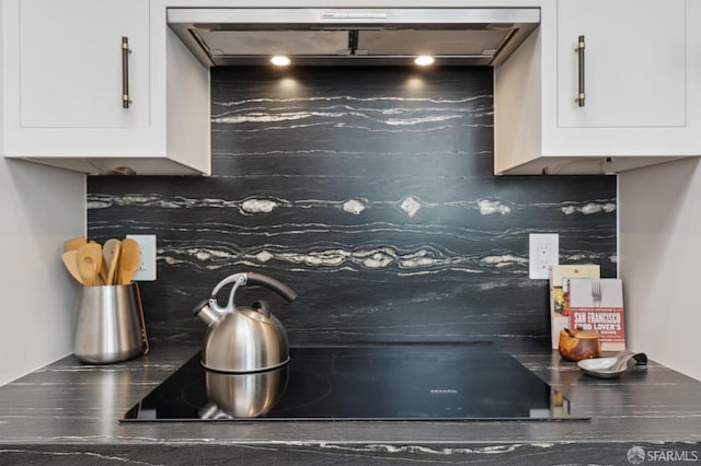 kitchen view of backsplash, dark countertops, white cabinets, and black electric stovetop