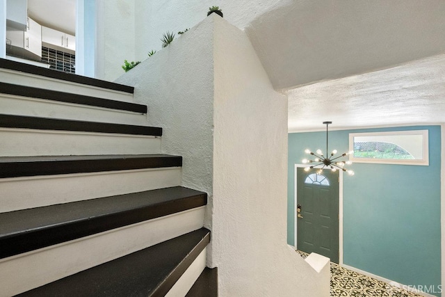 staircase with a textured ceiling, a textured wall, baseboards, and an inviting chandelier