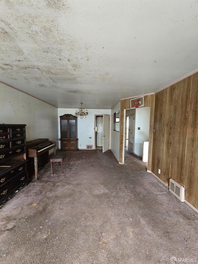 unfurnished living room with an inviting chandelier, carpet flooring, wood walls, and visible vents