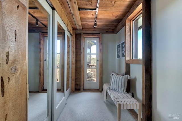 doorway to outside with light colored carpet, wooden ceiling, and rail lighting