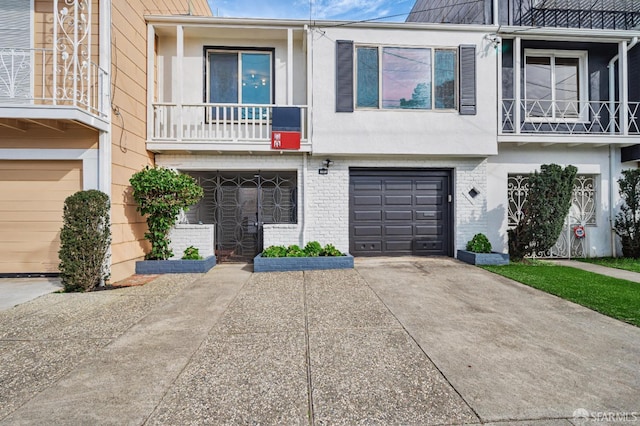 townhome / multi-family property with driveway, brick siding, a balcony, an attached garage, and stucco siding