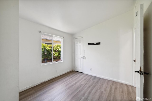 empty room with light hardwood / wood-style floors and vaulted ceiling