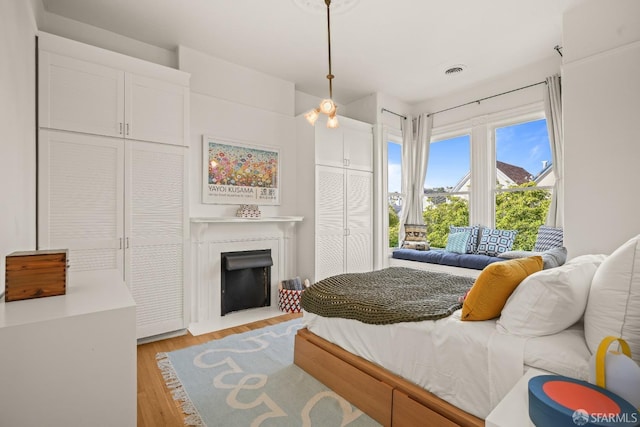 bedroom featuring light wood-type flooring, a fireplace with flush hearth, and visible vents