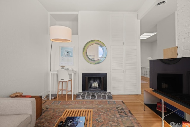 living area featuring a fireplace with raised hearth, wood finished floors, and visible vents