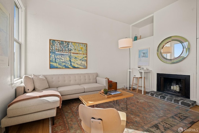 living room featuring dark wood-style floors, a fireplace with raised hearth, and plenty of natural light