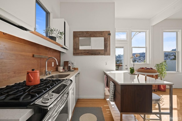 kitchen featuring light wood-style flooring, stainless steel appliances, a peninsula, a sink, and light countertops