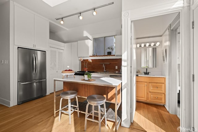 kitchen with light countertops, light wood-type flooring, stainless steel fridge, and a sink