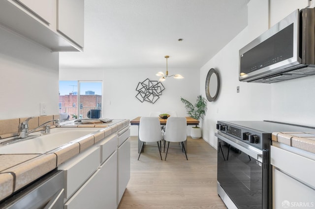 389 Belmont St Unit 306, Oakland, CA 94610 - kitchen with electric range, stainless steel microwave, tile countertops, light wood finished floors, and white cabinetry