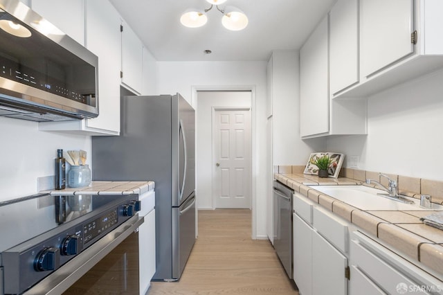 389 Belmont St Unit 306, Oakland, CA 94610 - kitchen featuring stainless steel appliances, white cabinetry, tile countertops, light wood-type flooring, and a chandelier