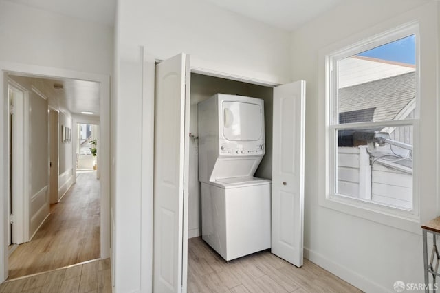 laundry room featuring baseboards, laundry area, light wood-style flooring, and stacked washer and clothes dryer