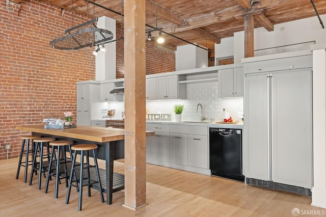 355 Bryant St Unit 411, San Francisco, CA 94107 - kitchen with black dishwasher, open shelves, a high ceiling, brick wall, and light wood-style flooring
