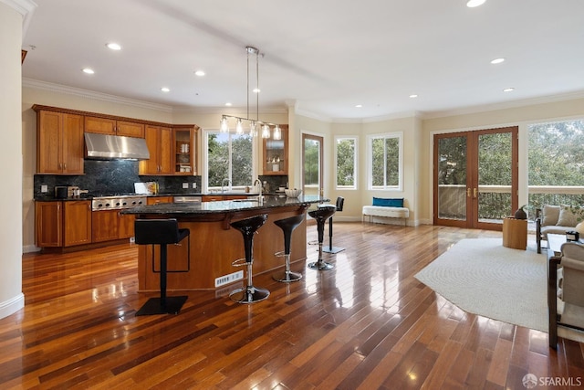 110 Sheridan Rd, Oakland, CA 94618 - kitchen featuring under cabinet range hood, brown cabinetry, dark wood-type flooring, a breakfast bar area, and ornamental molding