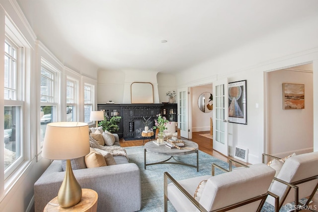 living area featuring baseboards, visible vents, wood finished floors, french doors, and a fireplace