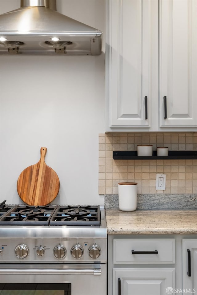 kitchen with white cabinetry, backsplash, light stone counters, extractor fan, and gas range