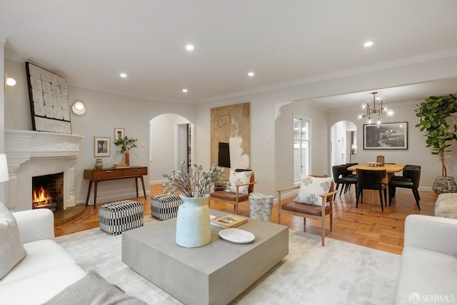 living room featuring an inviting chandelier, crown molding, a large fireplace, and light parquet flooring