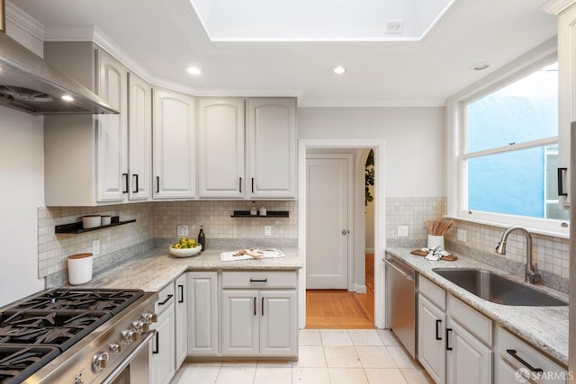 kitchen featuring sink, wall chimney range hood, appliances with stainless steel finishes, white cabinetry, and light stone countertops