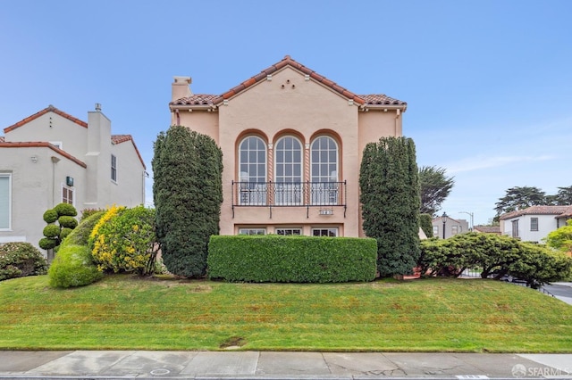 mediterranean / spanish-style house featuring a front yard, stucco siding, a tiled roof, and a chimney