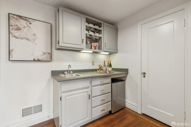 bar featuring dark wood finished floors, indoor wet bar, visible vents, a sink, and a textured wall