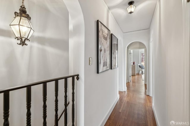 hall featuring arched walkways, dark wood-style flooring, and baseboards