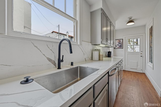 kitchen featuring gray cabinetry, decorative backsplash, dishwasher, a sink, and wood finished floors