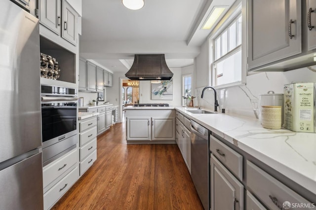 kitchen featuring range hood, a sink, appliances with stainless steel finishes, a peninsula, and gray cabinetry