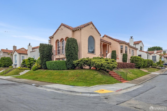 mediterranean / spanish-style home featuring a tiled roof, stucco siding, and a front lawn