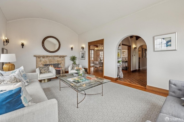 living room featuring baseboards, arched walkways, a fireplace, vaulted ceiling, and wood finished floors