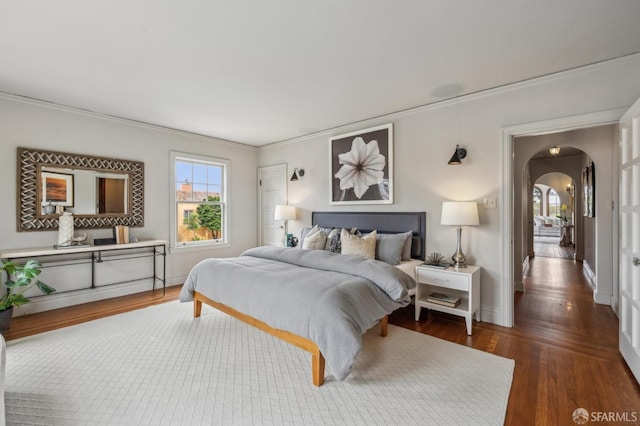 bedroom featuring crown molding, baseboards, arched walkways, and wood finished floors