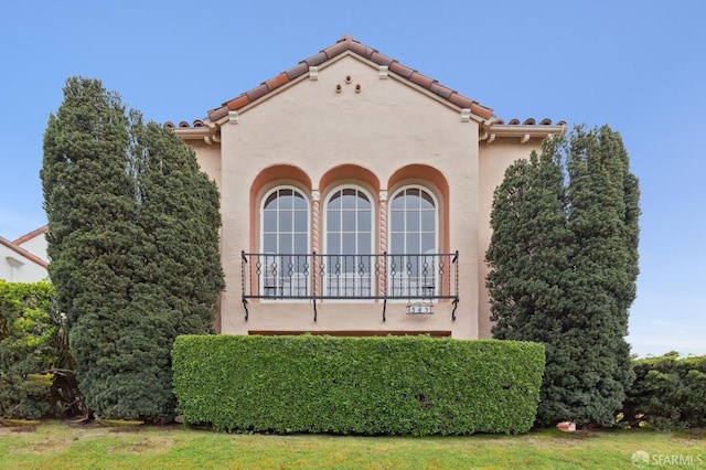 view of front of home featuring a tiled roof, a balcony, and stucco siding