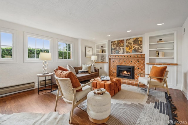 living area with a fireplace, a textured ceiling, wood finished floors, a baseboard radiator, and built in shelves