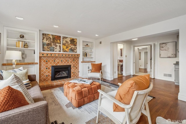 living room featuring a tiled fireplace, built in shelves, and baseboards