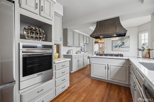 kitchen with dark wood finished floors, light stone countertops, gray cabinets, appliances with stainless steel finishes, and island exhaust hood