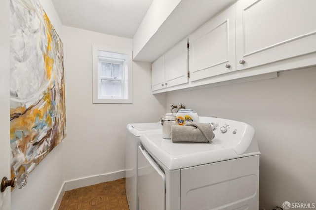 washroom featuring baseboards, washing machine and clothes dryer, and cabinet space