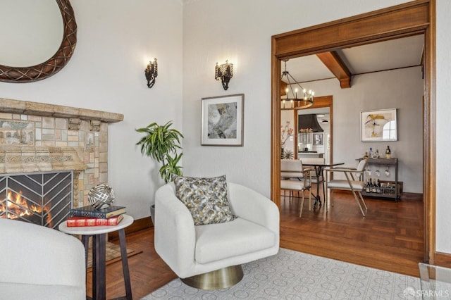 living room featuring beamed ceiling, a stone fireplace, a chandelier, and baseboards