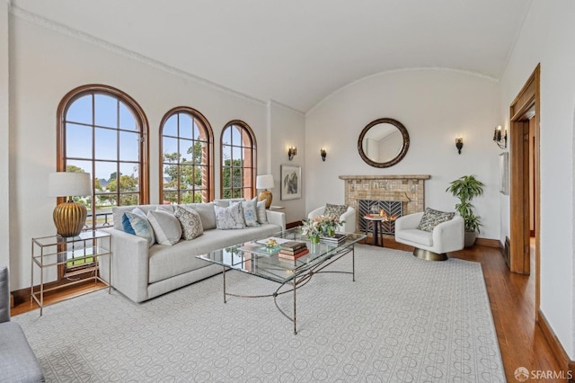 living room featuring lofted ceiling, baseboards, a lit fireplace, and wood finished floors
