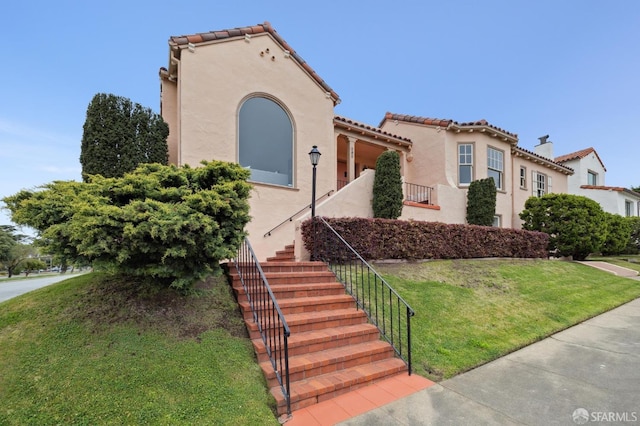 mediterranean / spanish house with a front yard, stucco siding, a tiled roof, and stairs