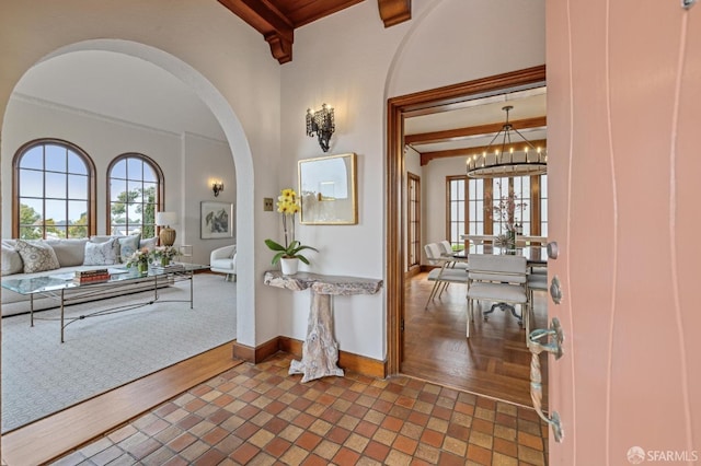 foyer featuring arched walkways, a notable chandelier, baseboards, and beam ceiling