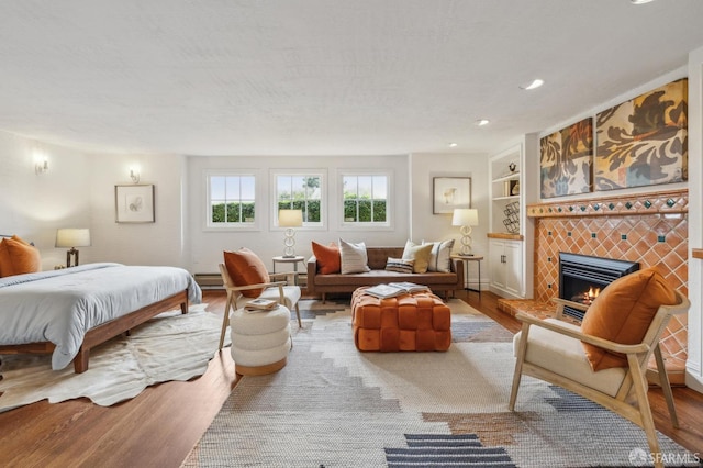 bedroom with recessed lighting, a tiled fireplace, a baseboard heating unit, and wood finished floors