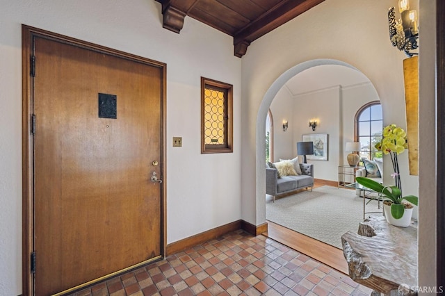 entryway featuring baseboards, arched walkways, wood ceiling, beamed ceiling, and tile patterned flooring