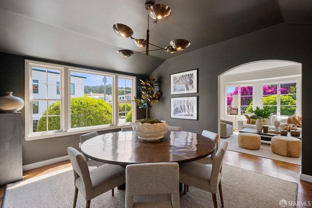 dining area with wood-type flooring, plenty of natural light, lofted ceiling, and a notable chandelier