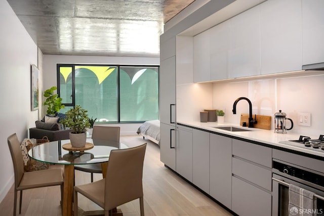 kitchen featuring light hardwood / wood-style floors, oven, white cabinetry, and sink