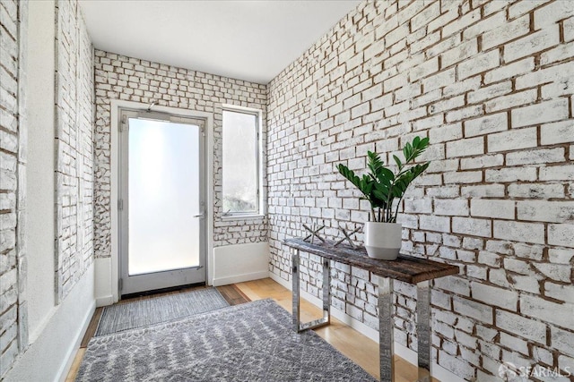 foyer entrance featuring baseboards, wood finished floors, and brick wall