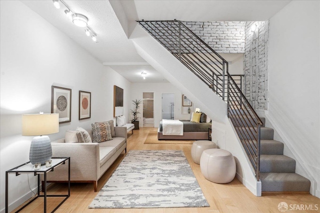 living room featuring stairs, track lighting, wood finished floors, and baseboards