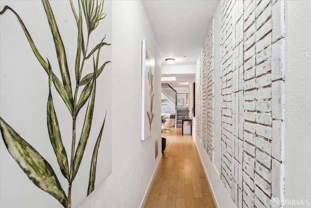 corridor featuring baseboards, wood finished floors, and brick wall