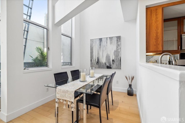 dining room with baseboards, light wood-style floors, and a towering ceiling